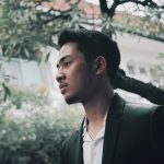 Portrait of a young man in a suit outdoors, framed by urban tree branches.